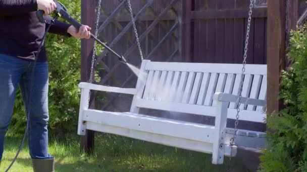 Male gardener removes white paint from a swing bench with high pressure washer — Stock Video