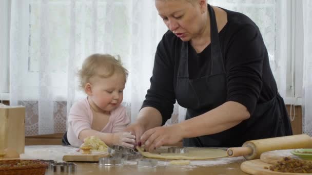 Granny cutting cookies of raw gingerbread dough with cute granddaughter — Stock Video