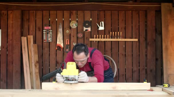 Trabajador de la madera procesa madera con una fresadora en su taller de carpintería — Vídeo de stock