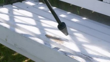 Adam yüksek basınçlı çamaşır makinesiyle zincirli banktaki boyayı çıkarıyor.