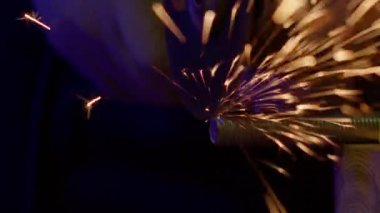 Tulumlu bir çilingir, metali öğütücüyle keser. Kıvılcımlar yavaş çekimde uçar.