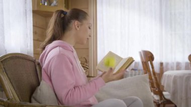 Kapüşonlu kadın kanepede oturup elma yerken kitap okuyor..