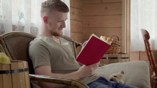 Beau étudiant au repos claquant à la maison, lisant le livre de papier — Video