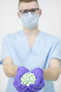 Gözlük takan ve maske takan genç ve yakışıklı stajyer bir avuç dolusu hap tutuyor.