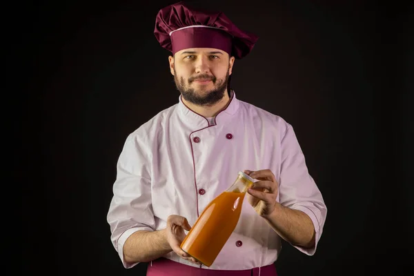Cocinero masculino barbudo en uniforme sosteniendo botella de plástico de jugo de frutas —  Fotos de Stock