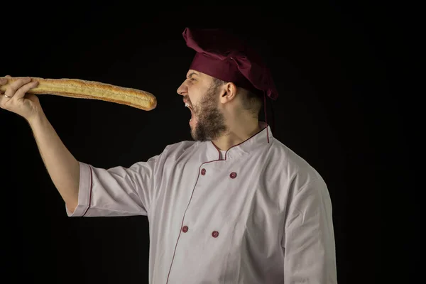 Panadero barbudo hanger hombre en uniforme abierto boca ancha para morder pan baguette —  Fotos de Stock