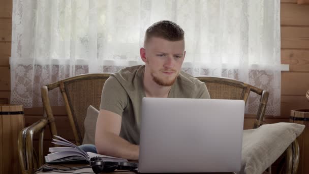 Joven hombre guapo trabaja en el ordenador portátil desde casa, estudiando en línea, la navegación por la red — Vídeos de Stock