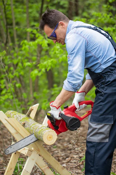 Maderero en uniforme de trabajo aserrando tronco de árbol en sierra con motosierra — Foto de Stock