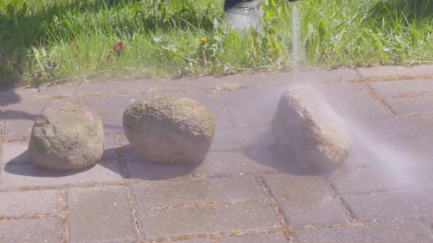 Человек моет камни и тротуарные плиты из грязи с помощью мойки высокого давления — стоковое видео