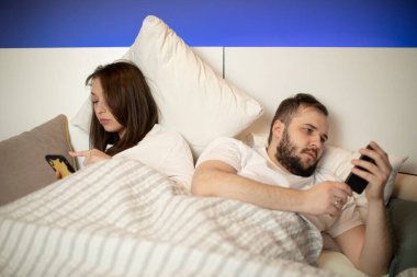 Esmer kız ve sakallı adam yataklarında akıllı telefonlarına bakıp geri dönüyorlar.