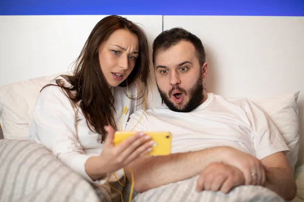Fille et son petit ami au lit étonnamment regarder smartphone avec écouteurs — Photo