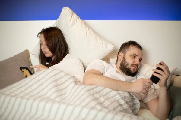 brunette girl and bearded guy looks into their smartphones in bed turning back