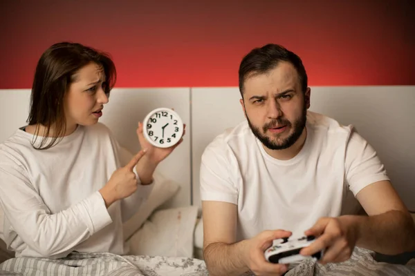 Fille pointe à horloge tandis que son petit ami joue à des jeux vidéo dans le lit la nuit — Photo