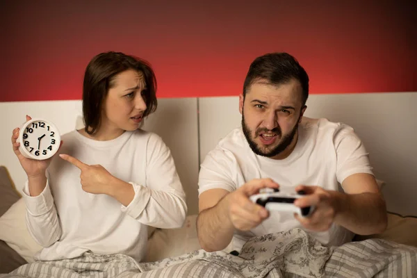 Fille points à horloge tandis que son petit ami joue console de jeu dans le lit la nuit — Photo