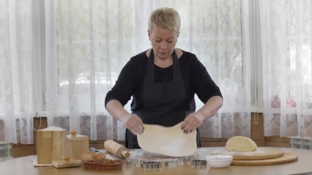 Orta yaşlı bir kadın un serpiştirilmiş bir masa üzerine ahşap raptiyeyle hamur yuvarlıyor. — Stok video