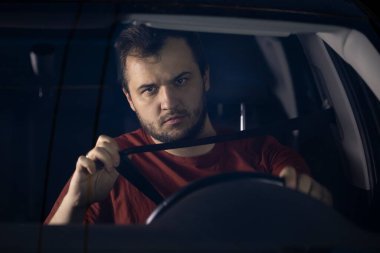 Genç sakallı adam emniyet kemerini arabaya takıyor. İyi yolculuklar.