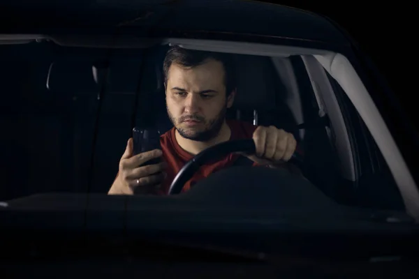 Hombre barbudo guapo se sienta en su coche y utiliza un teléfono inteligente — Foto de Stock