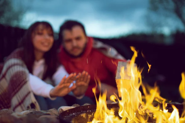 Portrait of happy lovely couple resting on nature. Woman warms her hands by fire