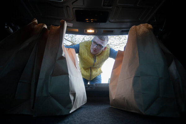 Male shopaholism concept. Handsome guy putting paper bags into car trunk