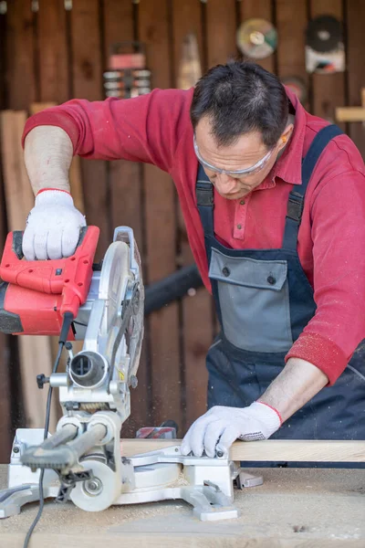 Un artisan mâle adulte coupe une planche de bois avec une scie à disque dans un atelier de menuiserie. — Photo