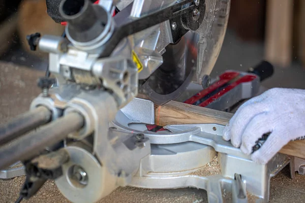 Charpentier coupe une poutre en bois avec une scie circulaire. Un gros plan des mains dans les gants. — Photo