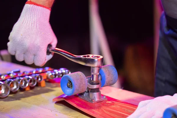 Mens hand in work glove fixing plastic child skateboard in home workshop — Stock Photo, Image