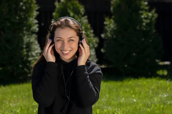 Mujer escucha música con auriculares sentados en el césped verde en el jardín cerca de la casa — Foto de Stock