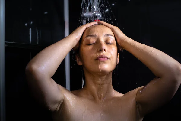 Kvinnan blundar och låter vatten skölja över henne medan hon duschar inomhus. — Stockfoto