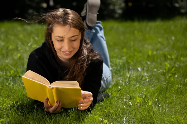 Bahçedeki yeşil çimlere uzanmış kitap okuyan genç bir kadının portresi.. — Stok fotoğraf