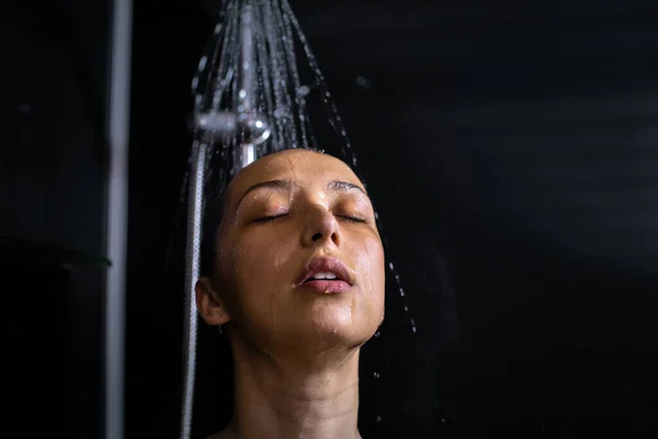 Giovane bella donna in piedi con gli occhi chiusi sotto la doccia, gocce d'acqua sul viso — Foto Stock