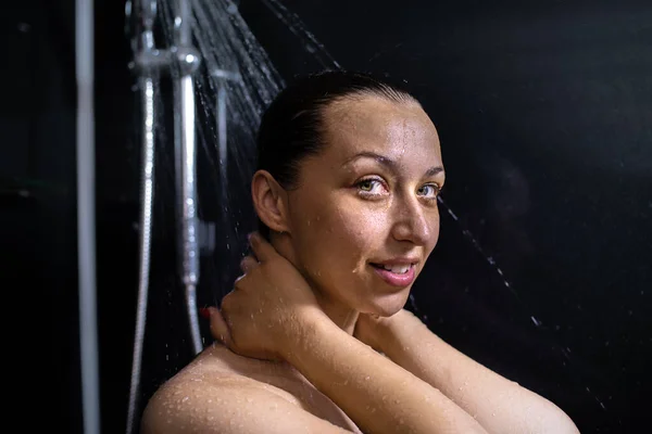 Χαμογελαστή γυμνή νεαρή γυναίκα απολαμβάνει τρεχούμενο νερό κάνοντας ντους κοιτάζοντας την κάμερα — Φωτογραφία Αρχείου