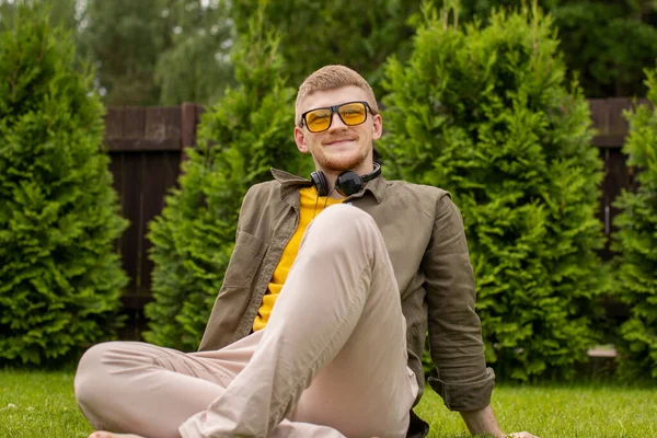 Joyeux jeune homme beau avec écouteurs assis sur l'herbe — Photo