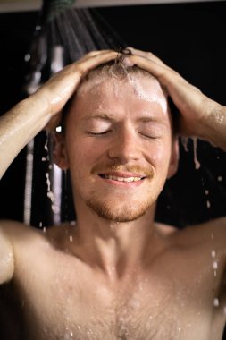 Genç, gülümseyen, sakallı, çıplak adam akan suyun tadını çıkarıyor.