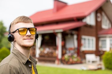 Sarı gözlüklü sakallı adam kulaklıkla müzik dinliyor.