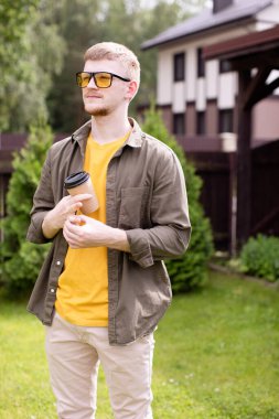 Güneşli bir yaz gününde tek kullanımlık kağıt bardak tutan sıradan giyinmiş bir adam.