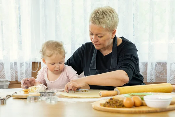 Sorrindo bonito bebê menina amassar massa para biscoitos na cozinha em uma mesa de madeira. — Fotografia de Stock