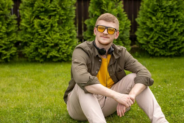 Descalzo joven se sienta pensativamente en la hierba verde con auriculares en el cuello —  Fotos de Stock