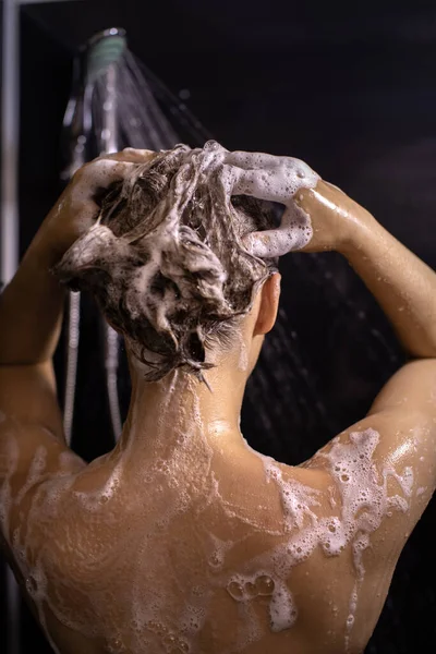Γυμνή νεαρή γυναίκα στέκεται στο μπάνιο αφρίζον σαμπουάν ή προϊόν περιποίησης μαλλιών — Φωτογραφία Αρχείου