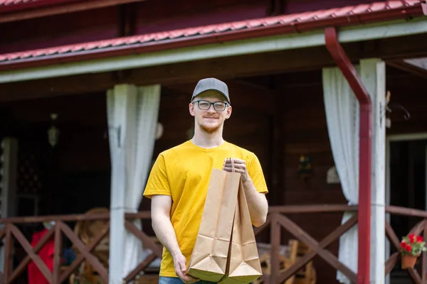 Young handsome delivery man holds biodegradable paper bags outdoors — Stock Photo, Image