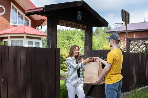 Delivery man handing paper bags to recipient in front of country house