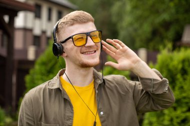 Kulaklıklı mutlu adam dışarıda gözleri kapalı pozitif müzik dinliyor.