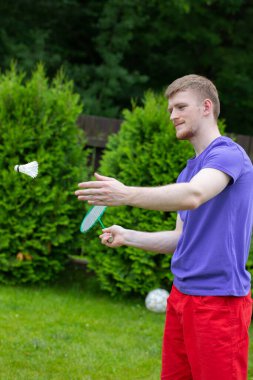 Genç güçlü beyaz adam raket ve mekikle badminton oynuyor.