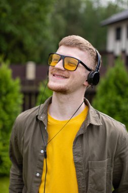 Kulaklıklı, olumlu gülümseyen adam dışarıda gözleri kapalı enerji müziğini dinliyor.