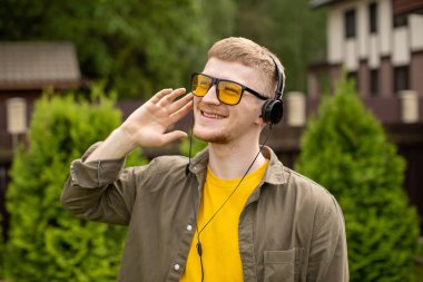 Kulaklıklı, elini kulağına dayayıp müzik dinleyen hippi bir adam.