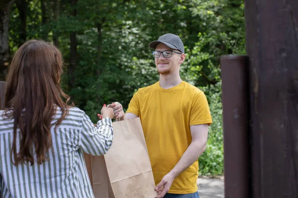 Handsome friendly deliver man handing paper bags with food to female customer