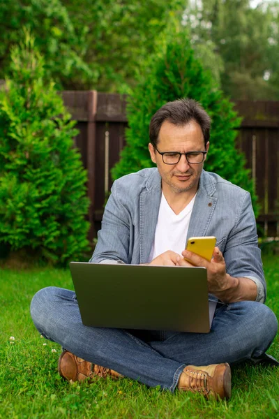 Hombre de negocios adulto que trabaja con computadora portátil y teléfono móvil al aire libre, multitarea — Foto de Stock