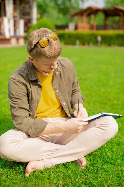 Genç hippi parkta çimlerde oturur, yapılacaklar listesi yapar, günlüğe planlar yazar. — Stok fotoğraf