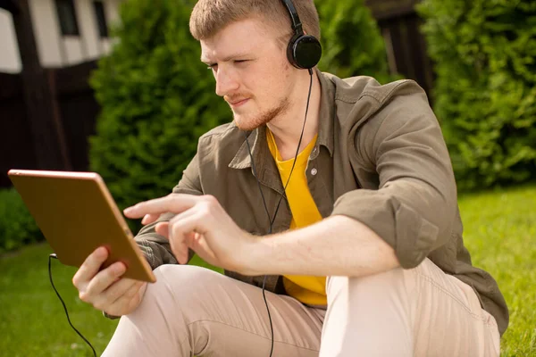 Estudiante inteligente con tableta digital escuchando podcast descansando en el parque en un día soleado — Foto de Stock