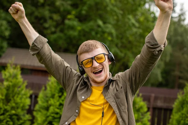 Fröhlich lächelnder Mann mit Kopfhörer hört positive Musik im Freien, Siegerkonzept — Stockfoto