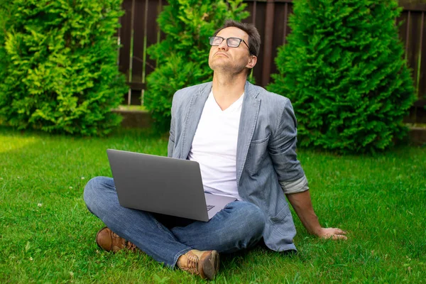 Hombre de negocios adulto se sienta al aire libre con el ordenador portátil, descansando meditando con los ojos cerrados — Foto de Stock